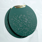 Bolsa redonda verde escura com textura abstrata cinza e alça dourada, sobre fundo branco