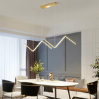Luminária pendente dourada moderna em formato geométrico iluminando mesa de jantar com cadeiras em ambiente interno