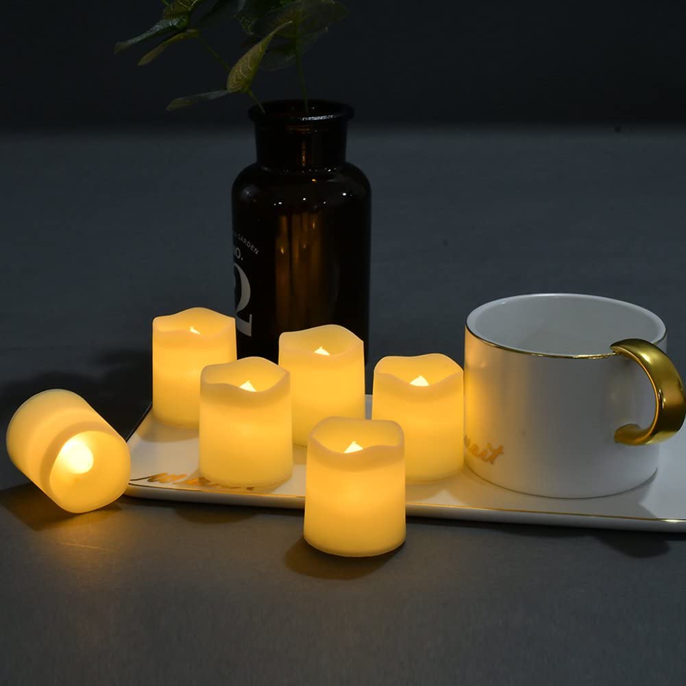 Velas LED amarelas brilhando em bandeja branca ao lado de caneca branca com alça dourada e vaso decorativo