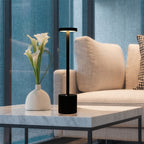 Abajur moderno preto e vaso branco com flores em mesa de mármore na sala com sofá bege