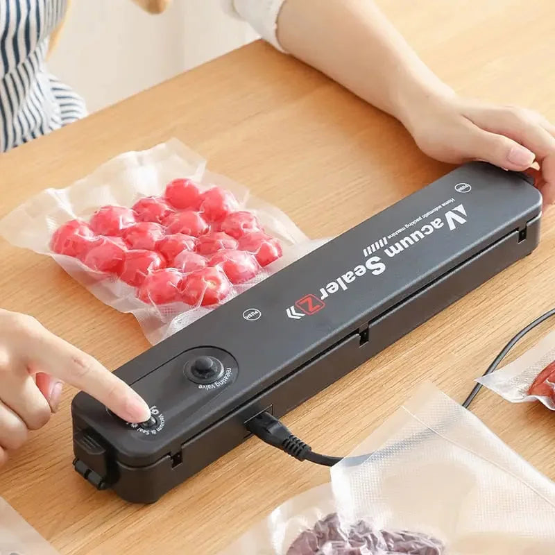 Seladora a vácuo portátil preta da Vácuum Sealer em uso na mesa com alimentos embalados a vácuo