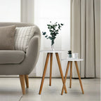 Mesa de centro nordica branca com pernas de madeira e vaso com folhagem ao lado de sofa cinza com almofadas